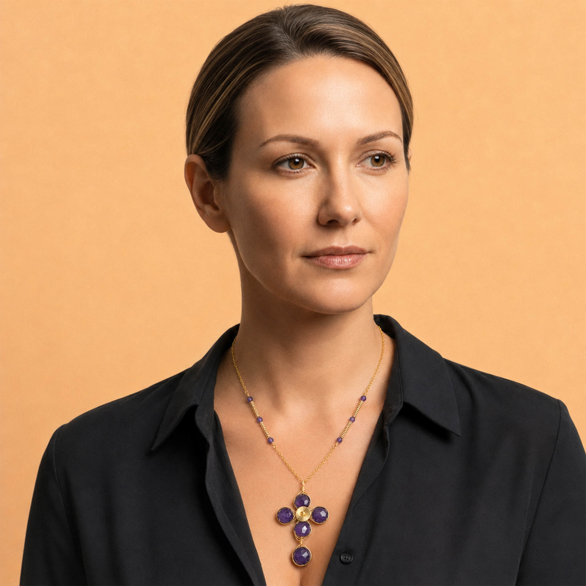 Model wearing a gold amethyst cross necklace with purple gemstone accents over a black blouse