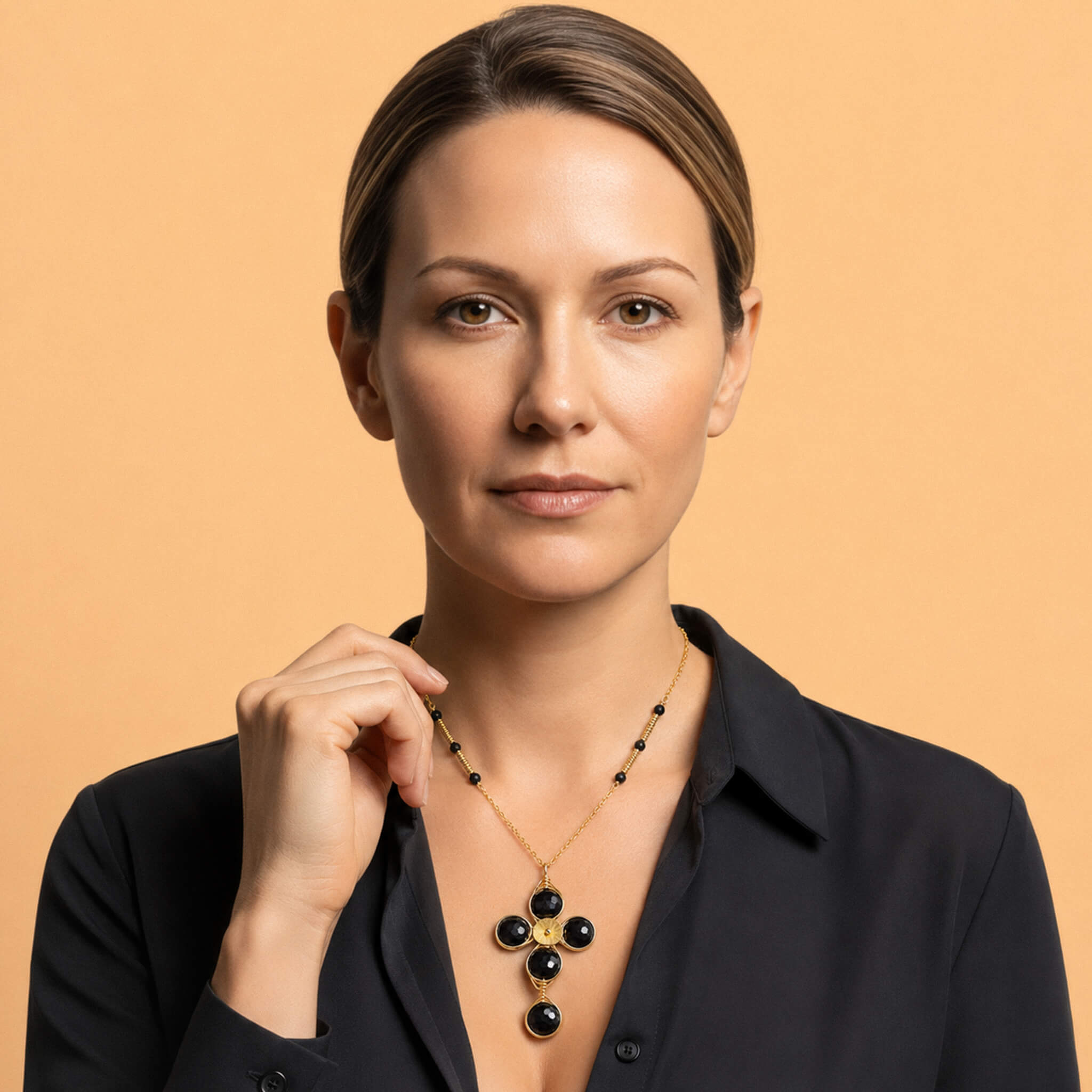 Woman wearing a gold garnet cross necklace with faceted dark red stones over a black blouse
