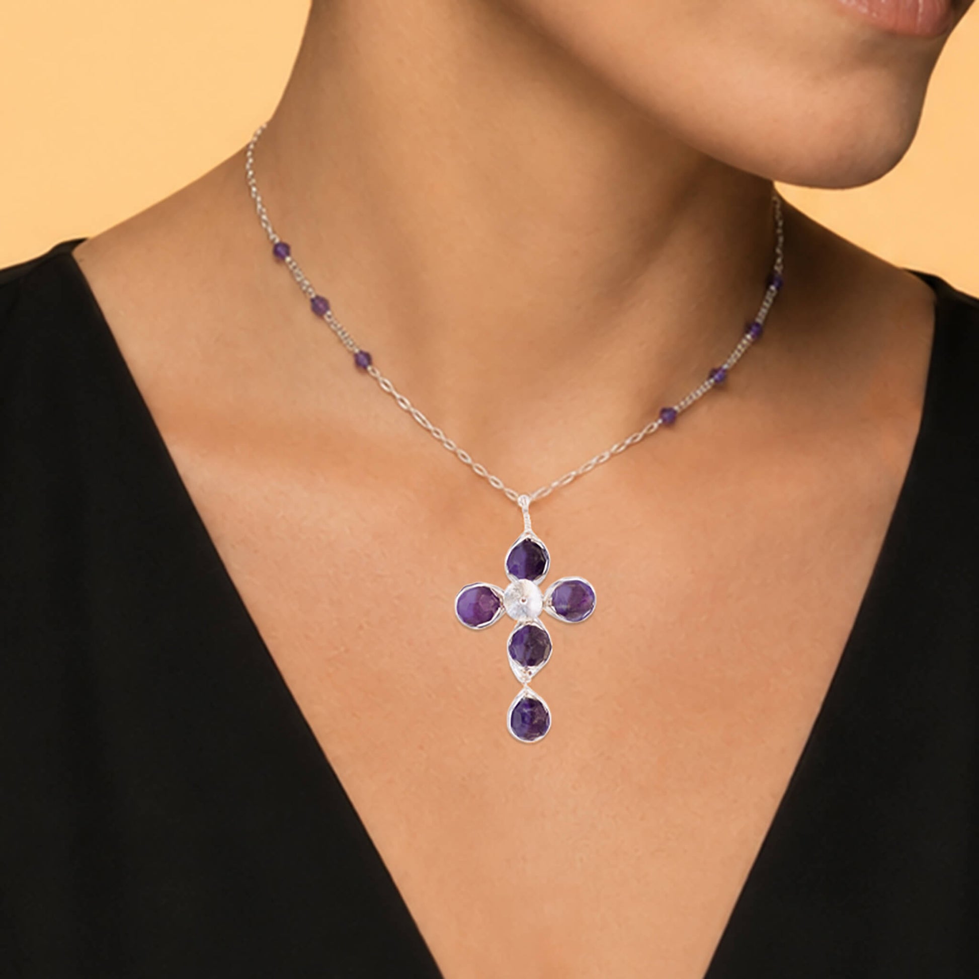 Close-up of a silver amethyst cross pendant showing five faceted stones and hand-worked wire detail