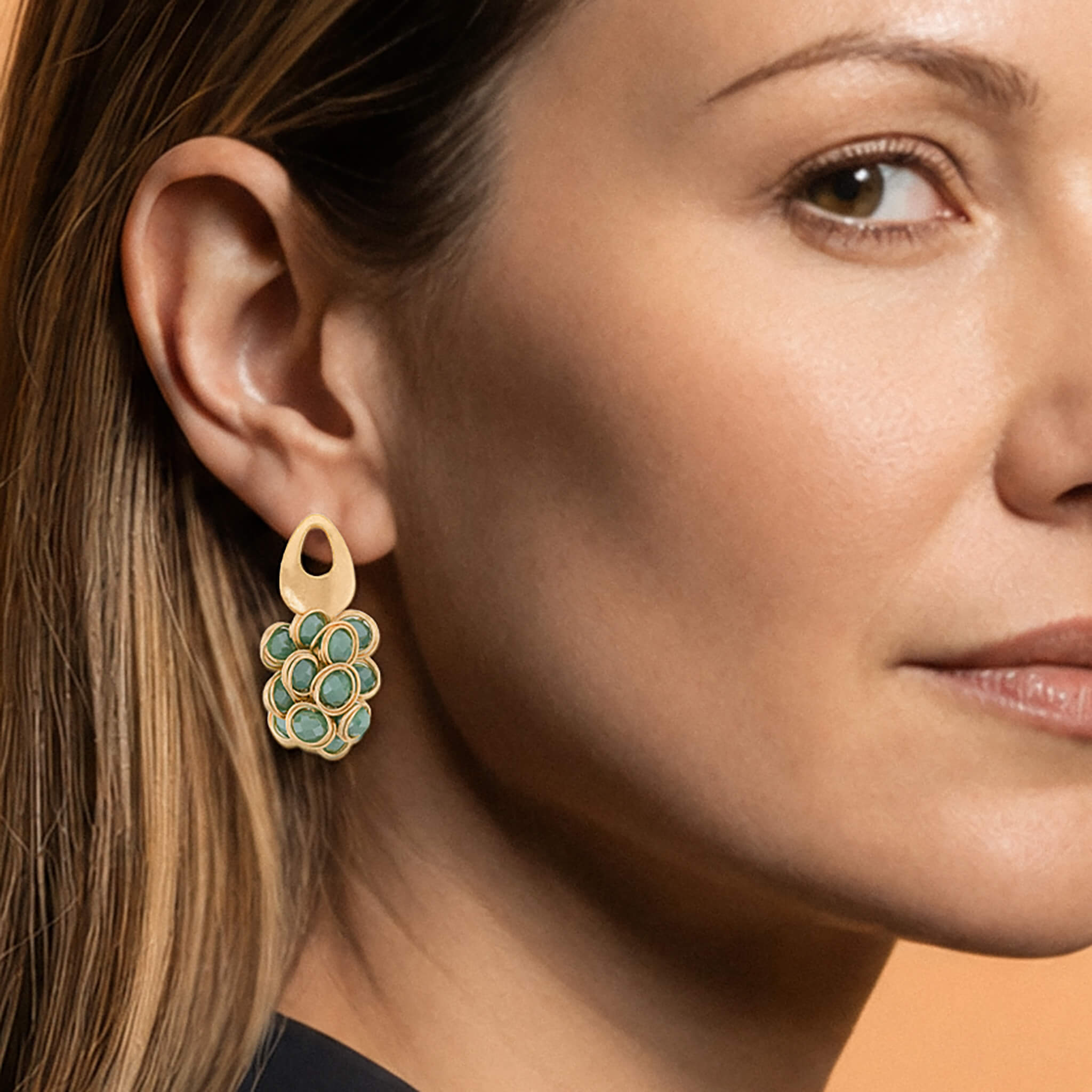 A close-up of a woman's ear wearing a gold dangle earring with a cluster of turquoise-blue stone accents.