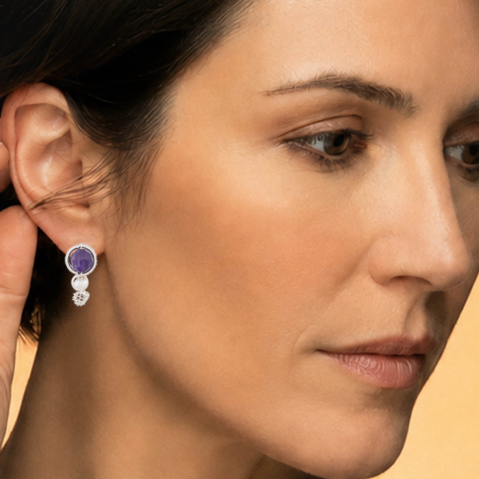 Close-up macro view of a model's ear showing a silver amethyst pearl drop earring, showcasing the tiered stone layout and detailed coiled wire framing.