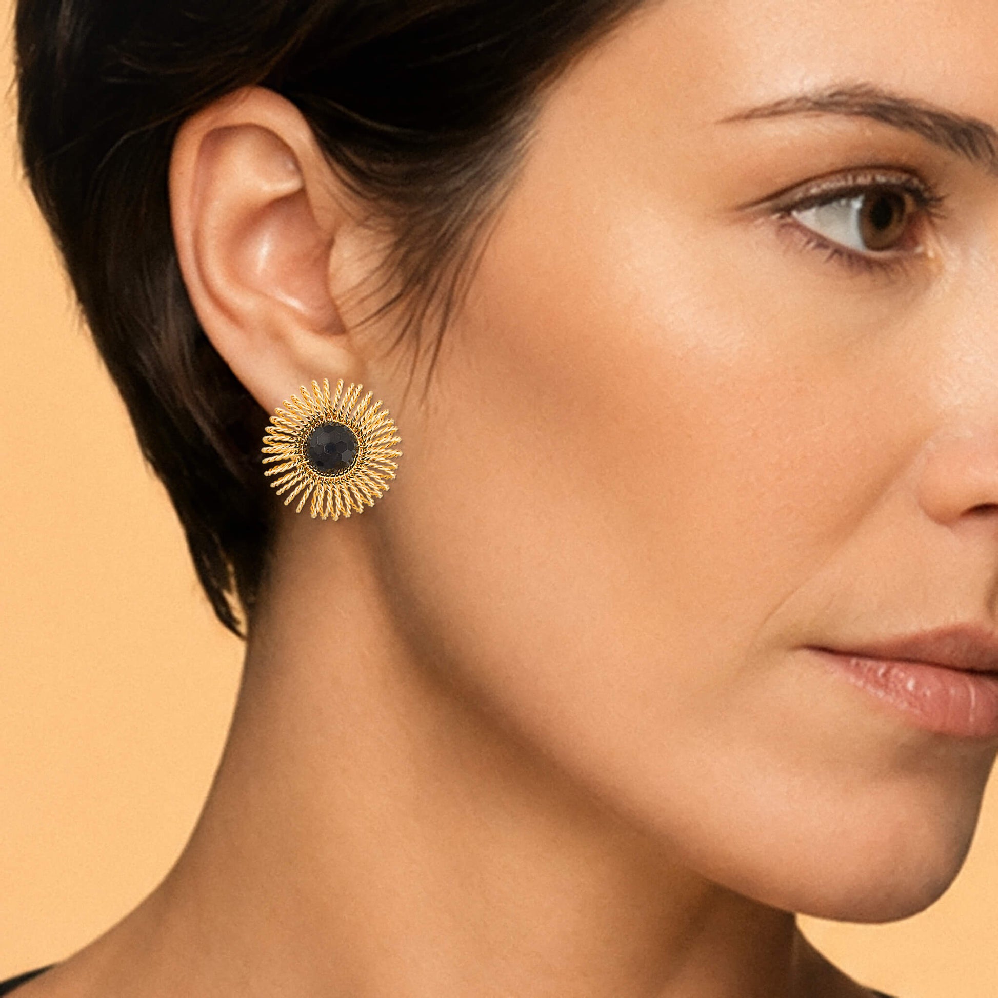 Close-up of a gold garnet sunburst stud earring showing its 1.5-inch scale and wire detail