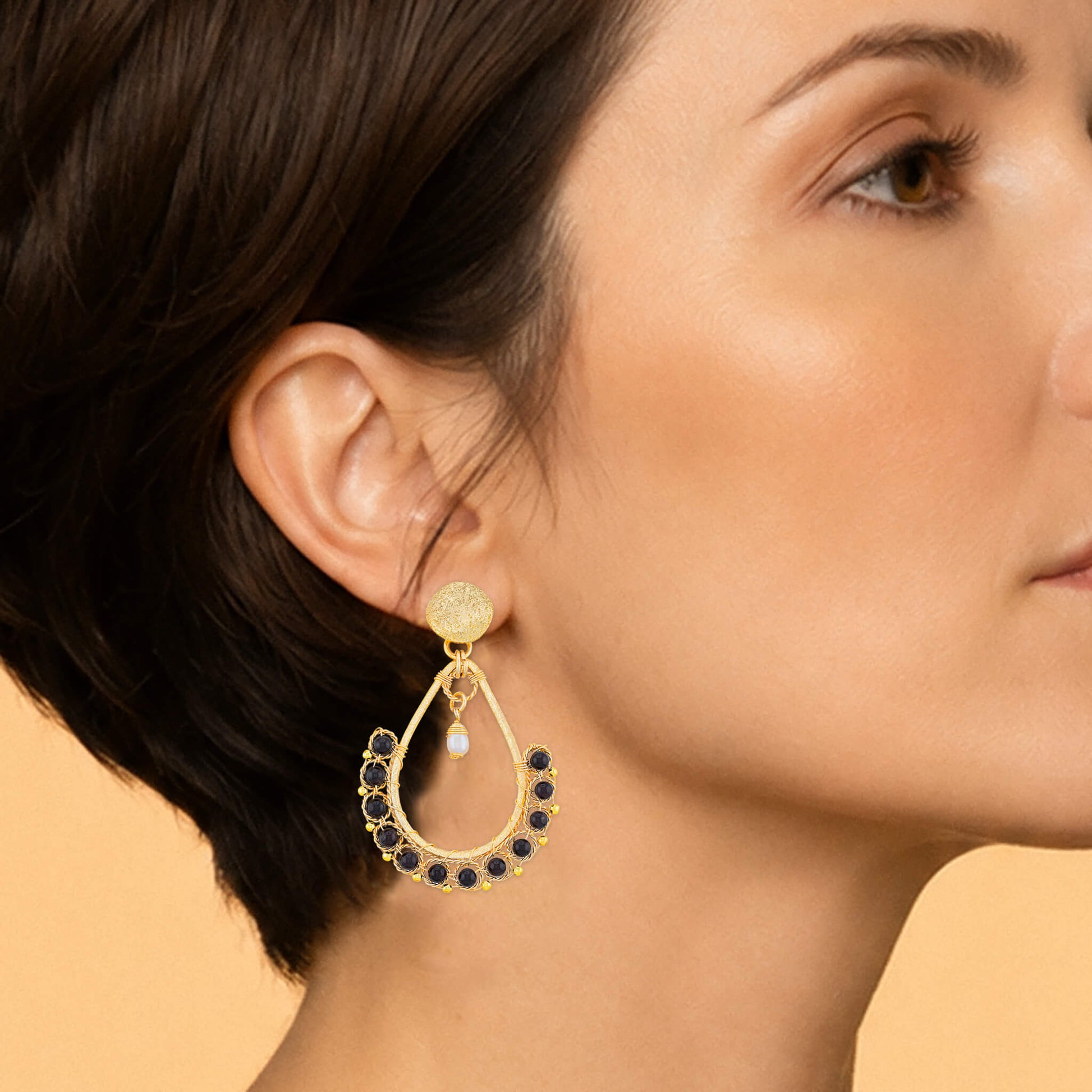 Close-up of a gold garnet teardrop earring showing faceted beads, pearl accent, and wire detail