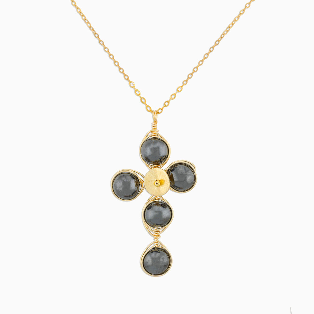 A gold cross pendant necklace featuring five dark gray round Hematite gemstones wrapped in gold wire, suspended from a delicate gold chain against a light gray background.