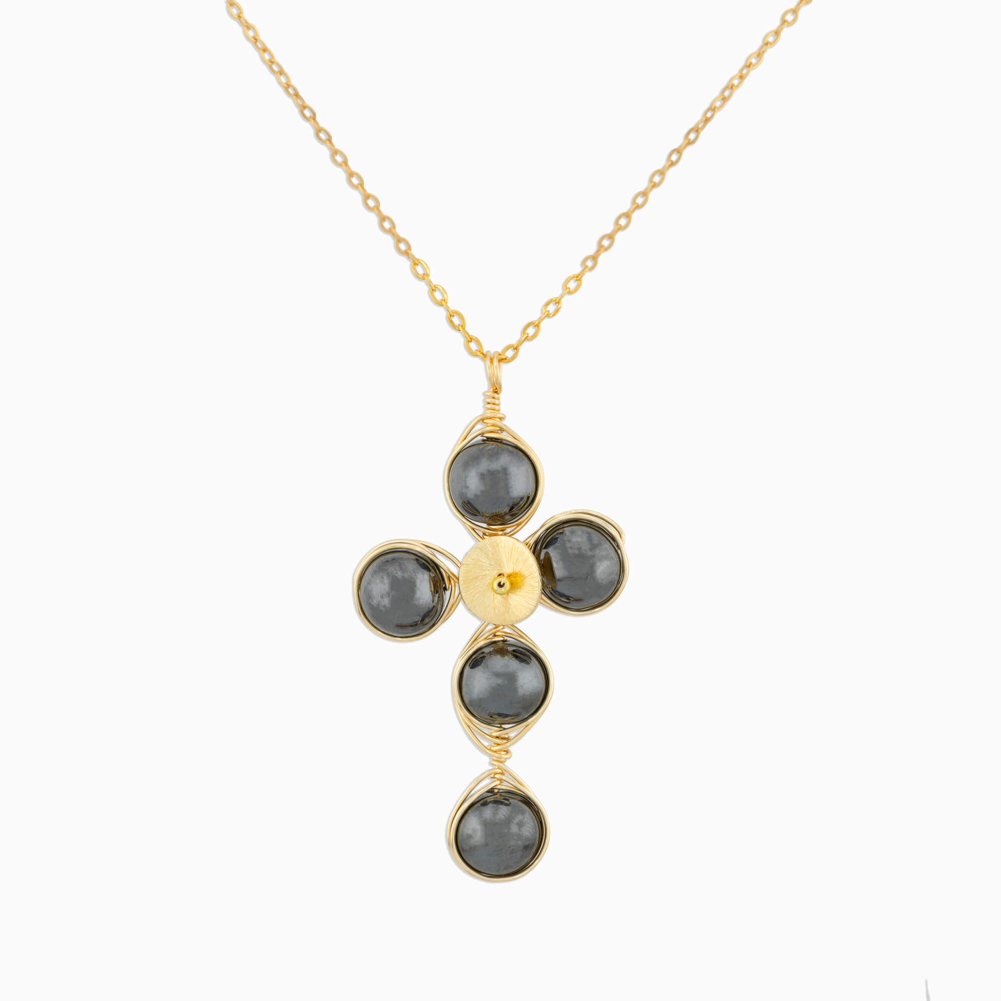 A gold cross pendant necklace featuring five dark gray round Hematite gemstones wrapped in gold wire, suspended from a delicate gold chain against a light gray background.
