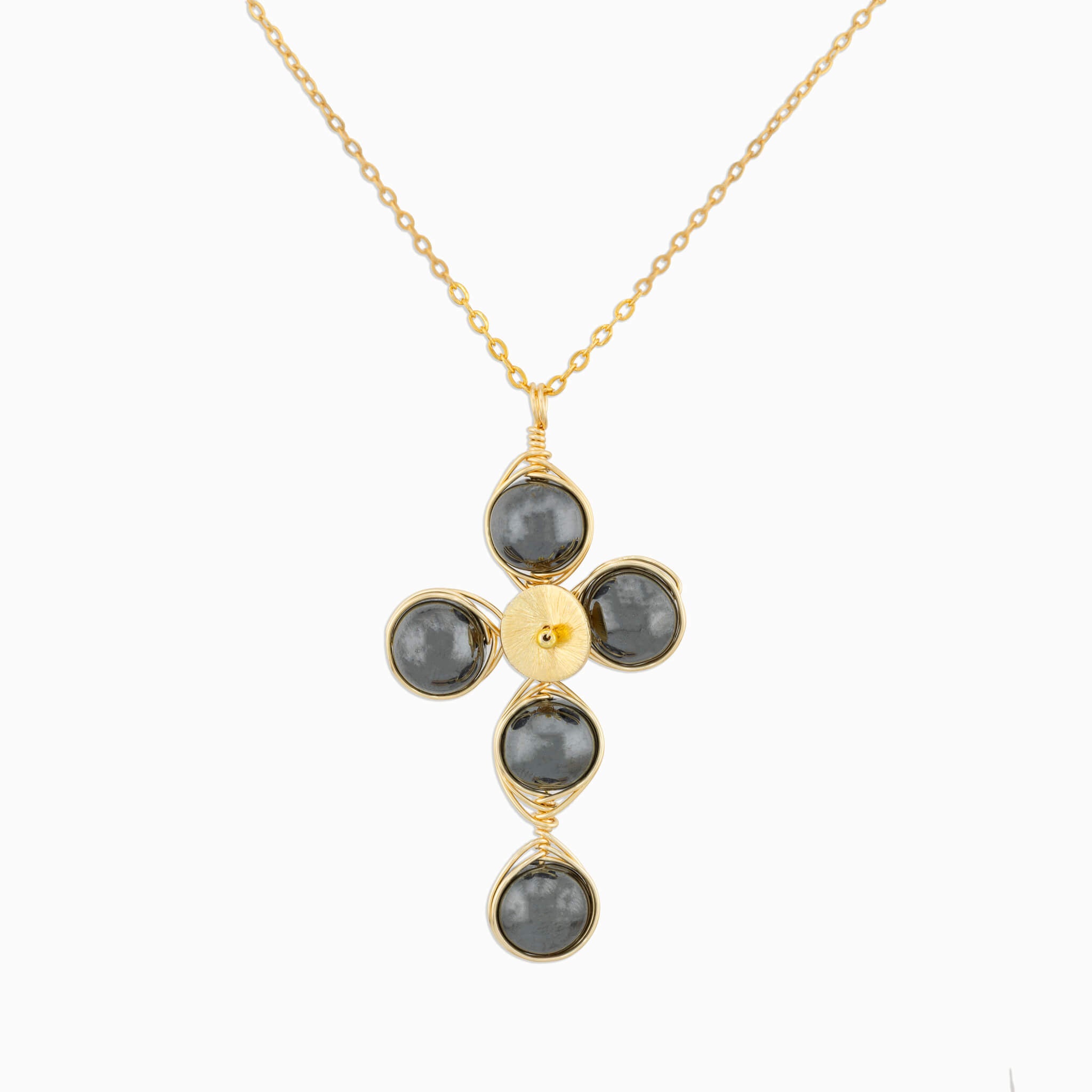 A gold cross pendant necklace featuring five dark gray round Hematite gemstones wrapped in gold wire, suspended from a delicate gold chain against a light gray background.