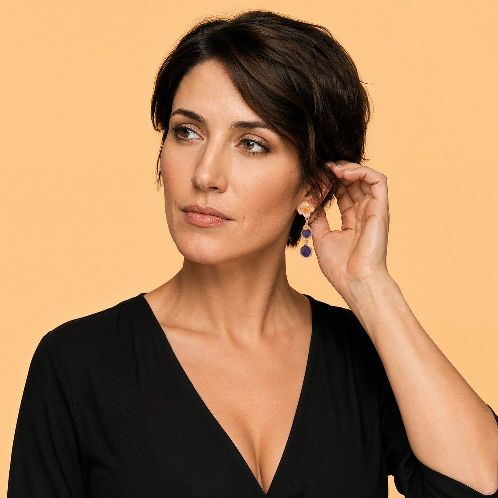 Model wearing gold amethyst flower drop earrings with a black top against a warm neutral background