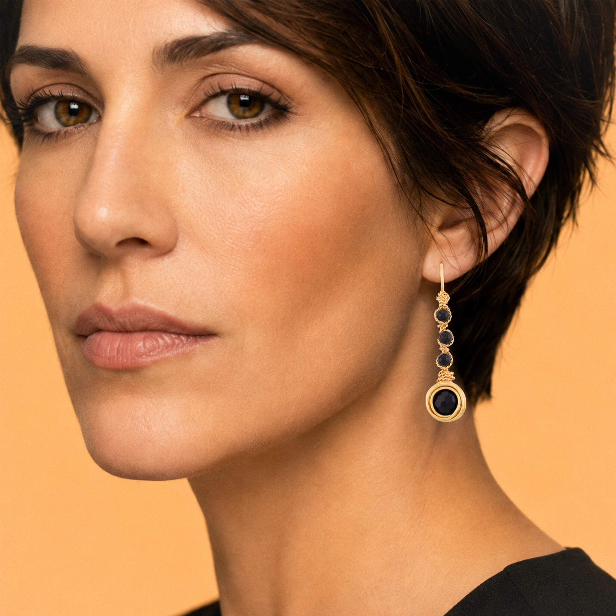 Macro close-up of a model's ear displaying a gold garnet drop earring, highlighting the deep crimson stones and detailed twisted-wire column.