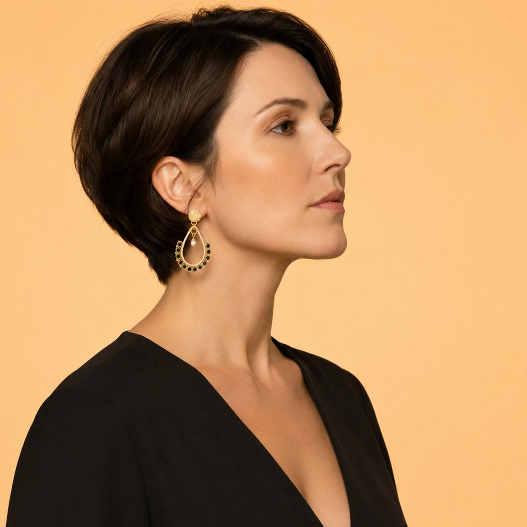 Woman wearing gold garnet teardrop statement earrings with a black top
