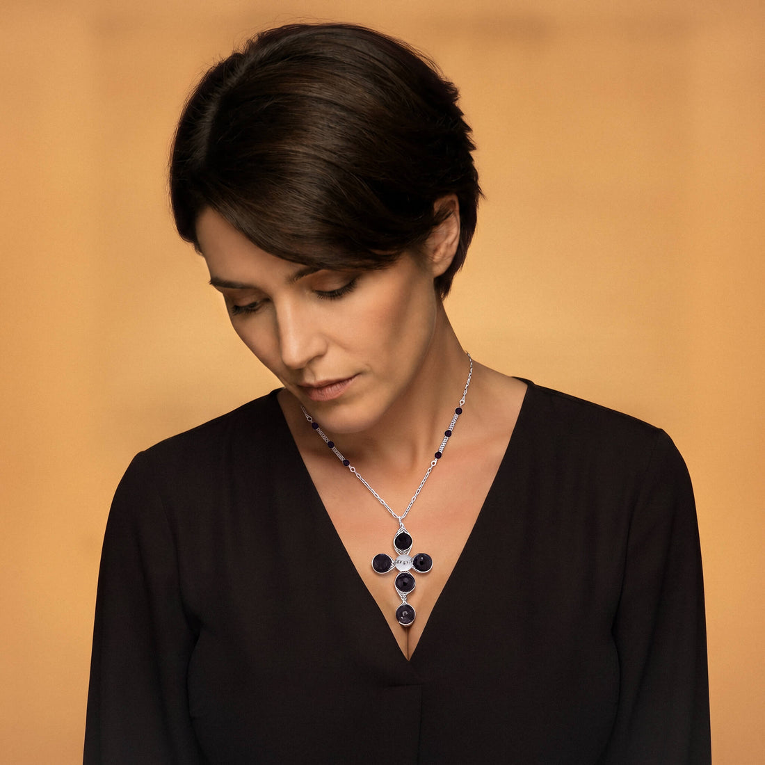 A silver cross pendant necklace featuring four round dark red garnet gemstones and a small silver disc at the center, suspended from a silver chain with small dark red garnet beads.