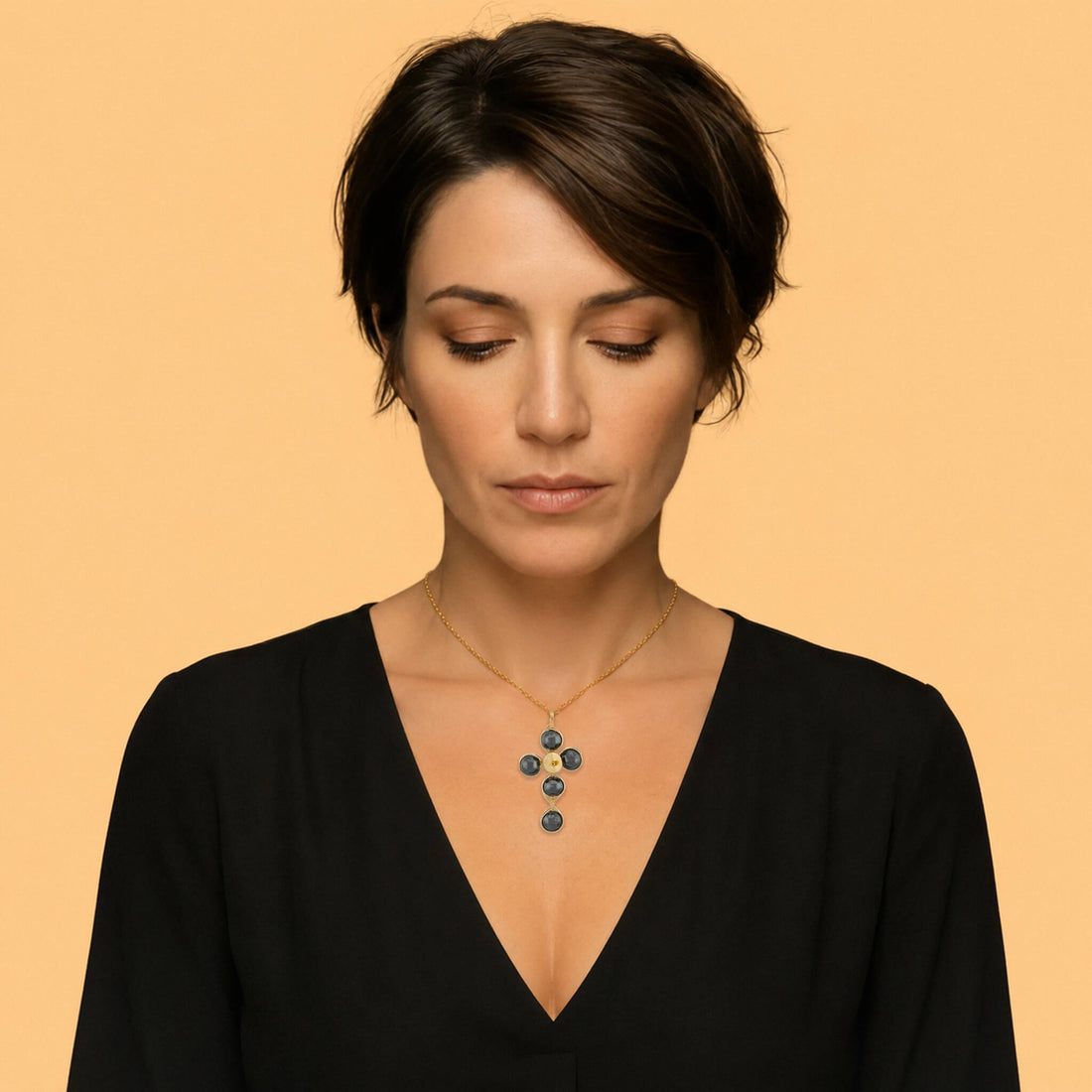 A gold cross pendant necklace featuring five dark gray round Hematite gemstones wrapped in gold wire, suspended from a delicate gold chain against a light gray background.