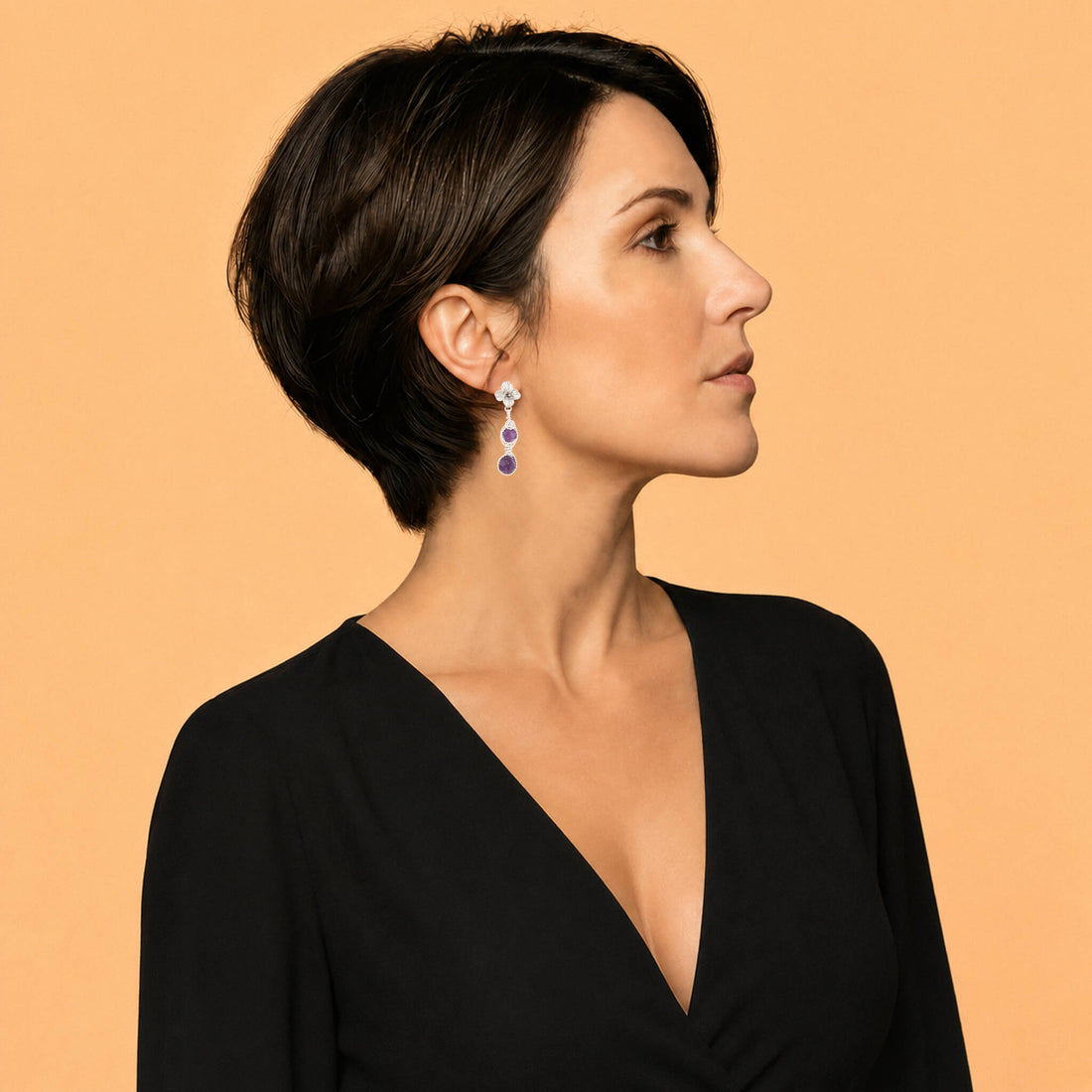 A pair of silver dangle earrings featuring textured flower studs, twisted wire details, and two round purple amethyst gemstones on each earring, set against a plain white background.