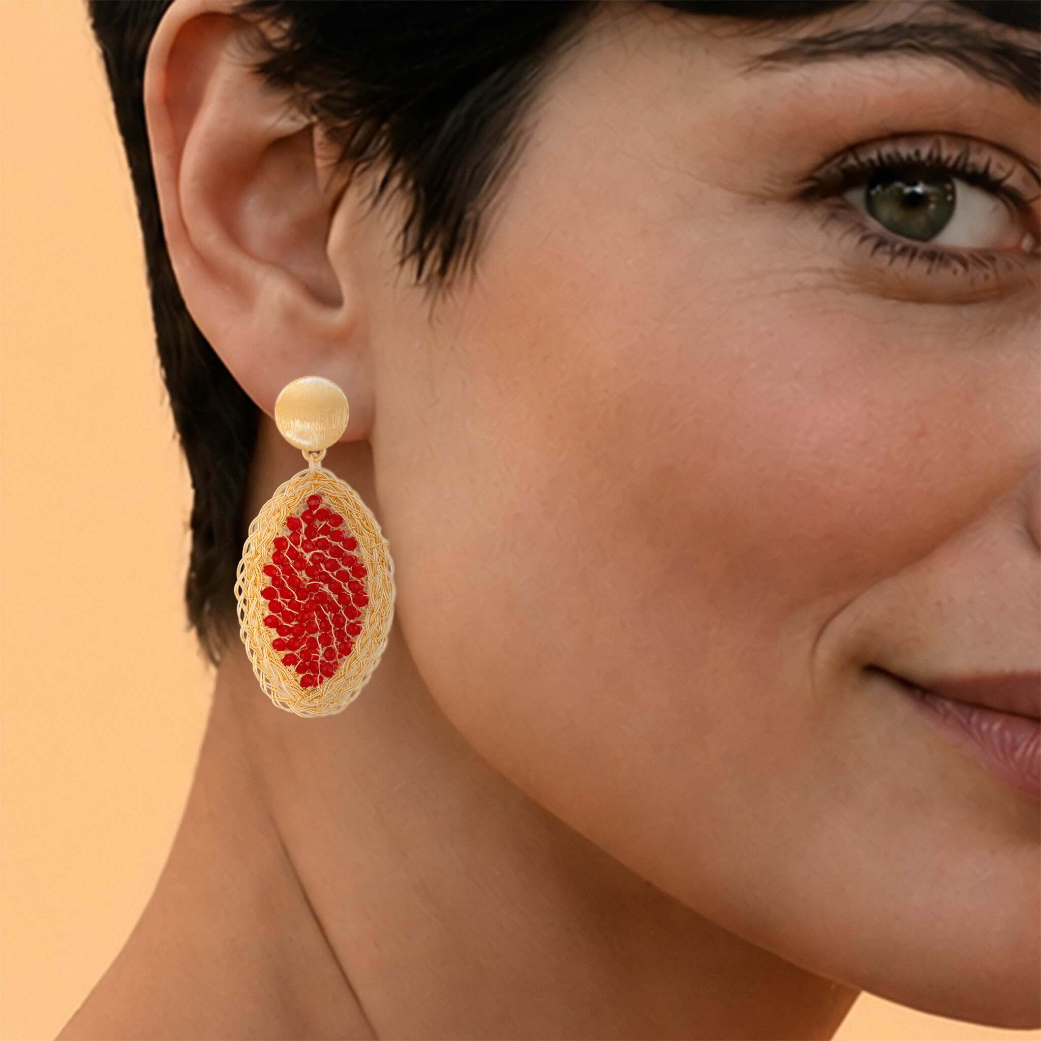 Macro close-up shot of a gold red crystal leaf earring on a model's ear, highlighting the braided metallic texture of the round stud post and the intricate mesh wirework enclosing the micro faceted red crystals