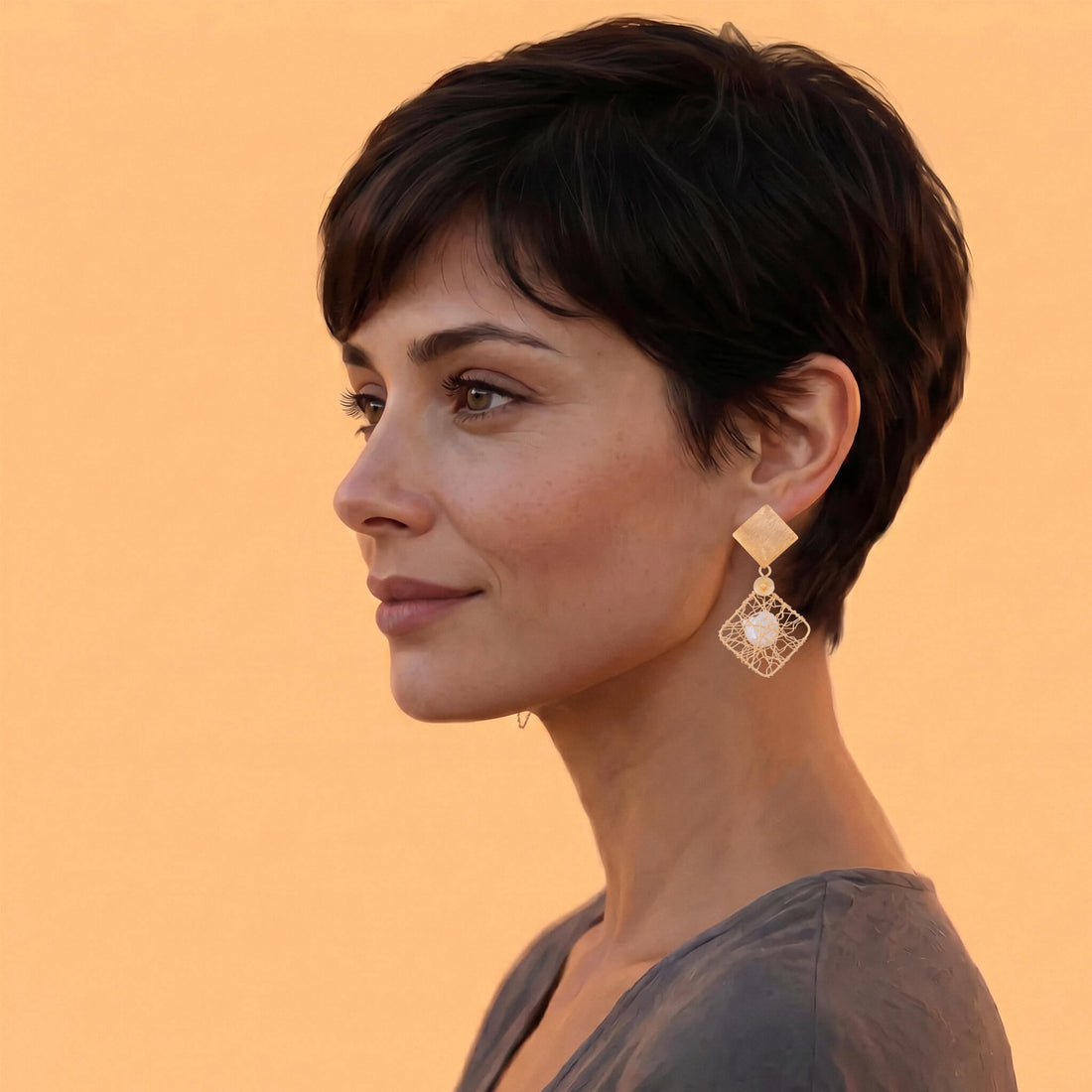 Pair of handcrafted gold geometric pearl earrings displaying a brushed square stud post suspending an open square wire-woven cage with a central freshwater pearl. The Nisha Earrings