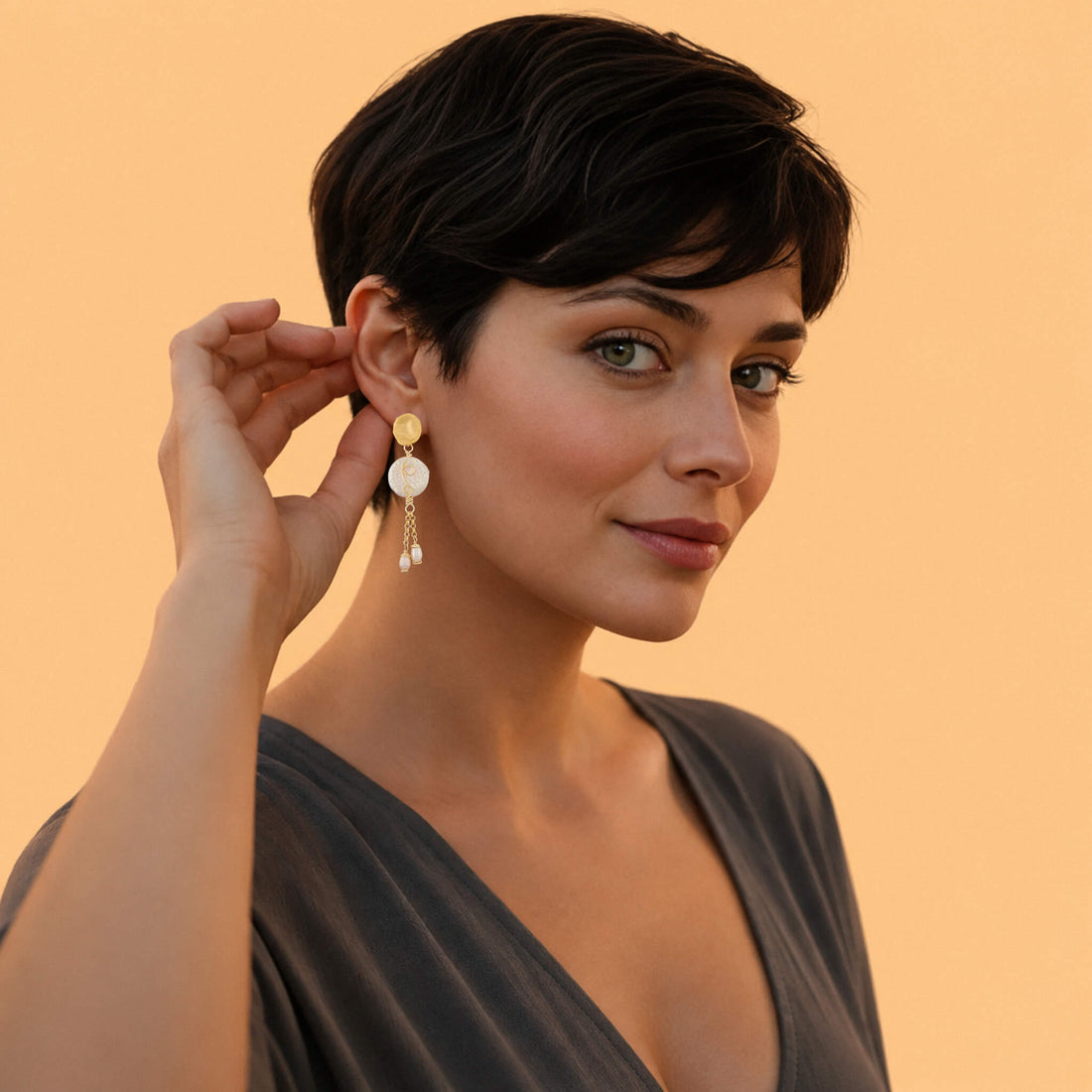 A pair of gold dangle earrings featuring textured circular discs, delicate chains, and small pearl-like beads, set against a plain white background.
