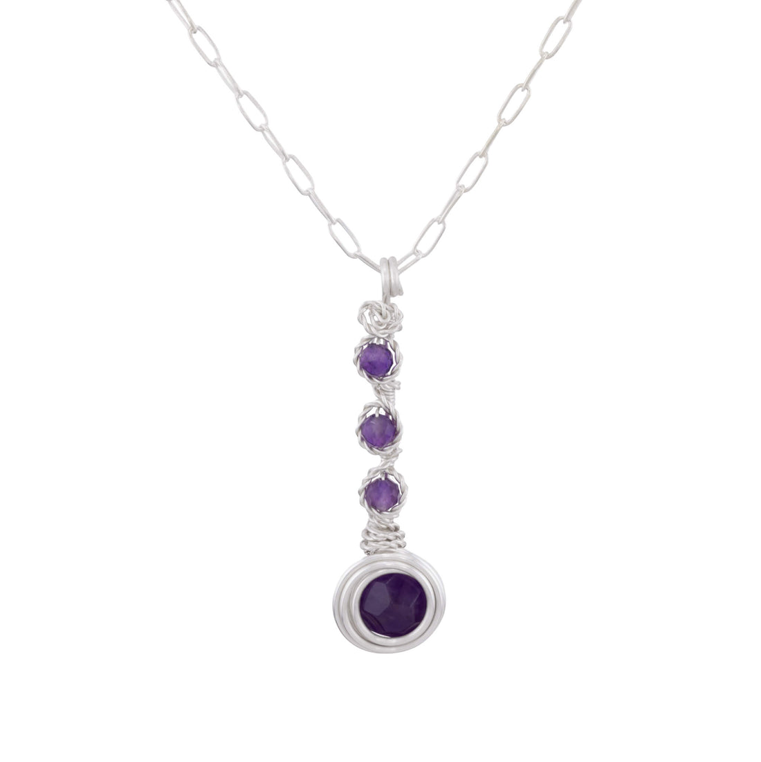 A silver paperclip chain necklace with a vertical drop pendant featuring three small round purple gemstones and a larger oval purple gemstone at the bottom, set against a plain white background.