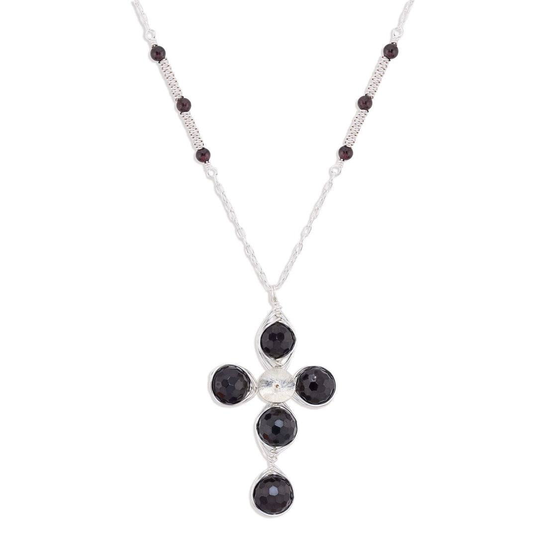 A silver cross pendant necklace featuring four round dark red garnet gemstones and a small silver disc at the center, suspended from a silver chain with small dark red garnet beads.