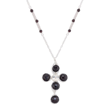 A silver cross pendant necklace featuring four round dark red garnet gemstones and a small silver disc at the center, suspended from a silver chain with small dark red garnet beads.